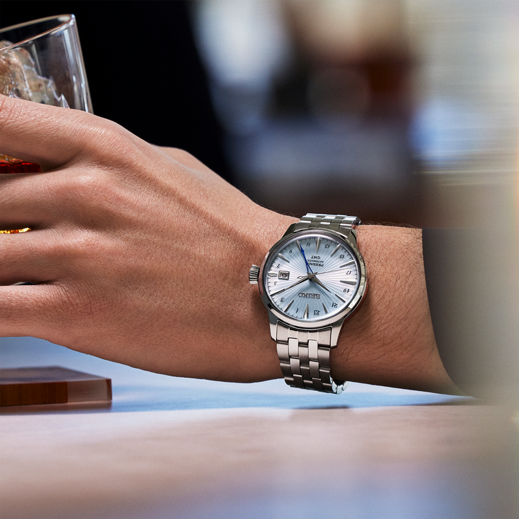 Hand wearing a silver watch with a blurred background